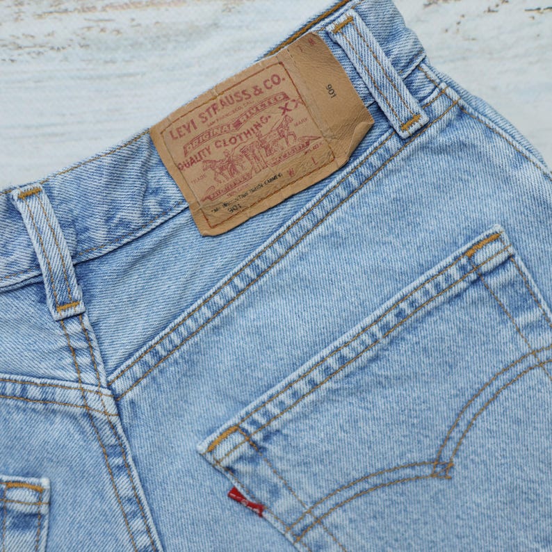 Puede incluir: Un par de pantalones vaqueros de mezclilla azul claro con un parche de cuero marr&oacute;n Levi Strauss & Co. en el bolsillo trasero. El parche tiene el texto "Levi Strauss & Co." y "Quality Clothing" impreso en &eacute;l. Los pantalones tienen un bolsillo trasero con una leng&uuml;eta roja que dice "Levi's".