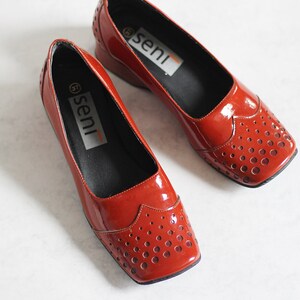 May include: A pair of red leather shoes with a perforated design and the word "seni" printed on the inside of each shoe.
