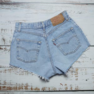 Puede incluir: Pantalones cortos de mezclilla azul claro con bordes deshilachados y un parche de Levi's en el bolsillo trasero.