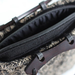 Puede incluir: Una bolsa negra con cremallera, con un asa de madera marr&oacute;n y un cord&oacute;n negro. La bolsa est&aacute; hecha de un tejido tejido con un patr&oacute;n blanco y negro.
