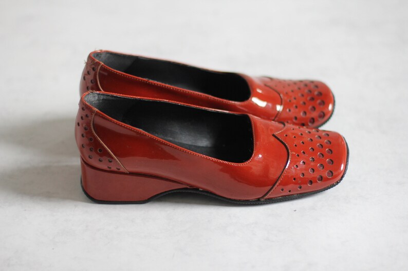May include: A pair of red patent leather shoes with a wedge heel and a perforated design.