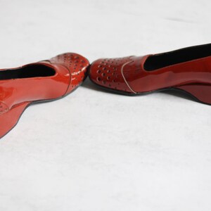 May include: A pair of red patent leather shoes with a wedge heel and cut-out detailing.