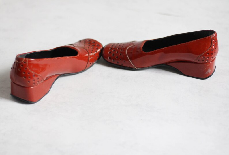 May include: A pair of red patent leather shoes with a wedge heel and cut-out detailing.