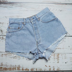 Puede incluir: Pantalones cortos de mezclilla azul claro con bordes deshilachados. Los pantalones cortos tienen cintura alta y un dise&ntilde;o cl&aacute;sico de cinco bolsillos.