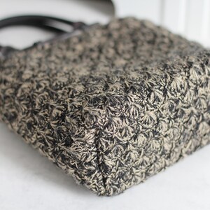 Puede incluir: Un bolso tote peque&ntilde;o, negro y beige con un patr&oacute;n floral. El bolso tiene dos asas negras.
