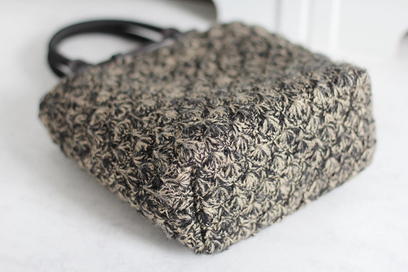 Puede incluir: Un bolso tote peque&ntilde;o, negro y beige con un patr&oacute;n floral. El bolso tiene dos asas negras.
