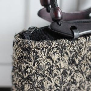 Puede incluir: Un bolso tejido negro y marr&oacute;n con una cremallera negra y un asa de madera con detalles negros.