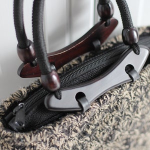 Puede incluir: Una bolsa de mano de punto marr&oacute;n y negro con asas de madera y cierre de cremallera negro.