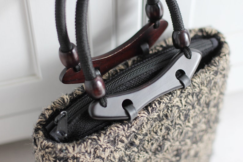 Puede incluir: Una bolsa de mano de punto marr&oacute;n y negro con asas de madera y cierre de cremallera negro.
