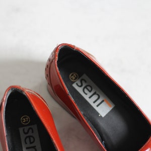 May include: A pair of red leather shoes with a black insole. The shoes have a small gold circle with the number 37 on the insole. The brand name "seni" is printed on the insole of the shoe.