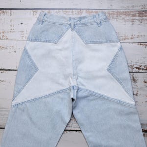 Op de afbeelding: Lichtblauwe spijkerbroek met een groot sterontwerp op de achterkant. De ster heeft een lichtere blauwtint, wat een contrasterend effect creëert. De jeans heeft een klassiek ontwerp met vijf zakken en een hoge taille.