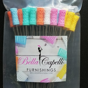 May include: A package of 12 colorful hair rollers with metal pins. The rollers are made of a soft, flexible material and have a textured surface. The package includes a label that says "Bella Capelli Furnishings" and "bellacapelliusa.com".