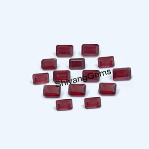 May include: A collection of rectangular, deep red gemstones, possibly rubies, arranged on a white surface. The gemstones are cut with a rectangular shape and have a polished, reflective surface. The text "ShivangGems" is visible.