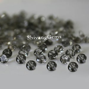 May include: A collection of black and clear round gemstone beads with black inclusions. The beads are scattered on a white surface. ShivangGems is printed in the center of the image.