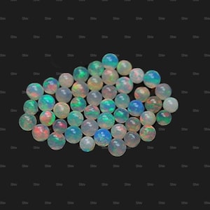 May include: A collection of iridescent opal gemstones, each a small sphere with a milky white base and flashes of colour including blue, green, and red. The opals are scattered against a dark background.