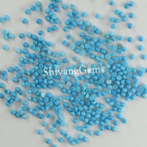 Könnte beinhalten: Eine große Menge kleiner, runder, türkisblauer Edelsteinperlen. Die Perlen sind auf einer weißen Oberfläche verstreut.