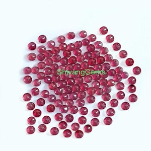 Może przedstawiać: Kolekcja małych, okrągłych, fasetowanych kamieni szlachetnych w różnych odcieniach czerwieni i różu. Kamienie szlachetne są rozrzucone na białej powierzchni. Tekst "ShivangGems" jest widoczny na środku obrazu.