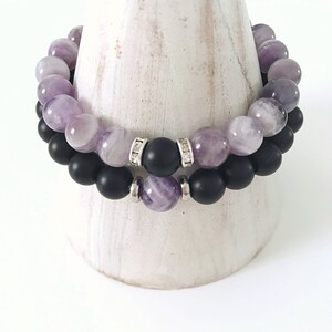May include: Two bracelets, one with purple amethyst beads and the other with black onyx beads. The amethyst bracelet has silver spacers with small clear crystals.