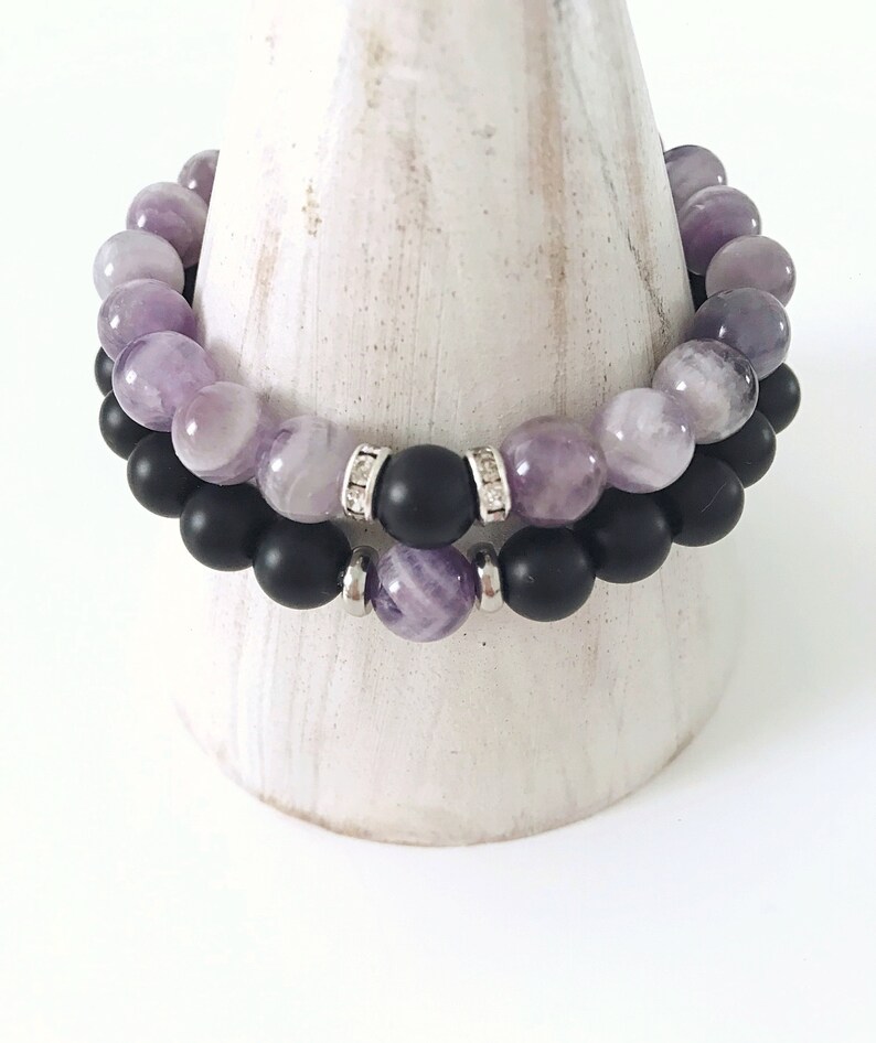 May include: Two bracelets, one with purple amethyst beads and the other with black onyx beads. The amethyst bracelet has silver spacers with small clear crystals.