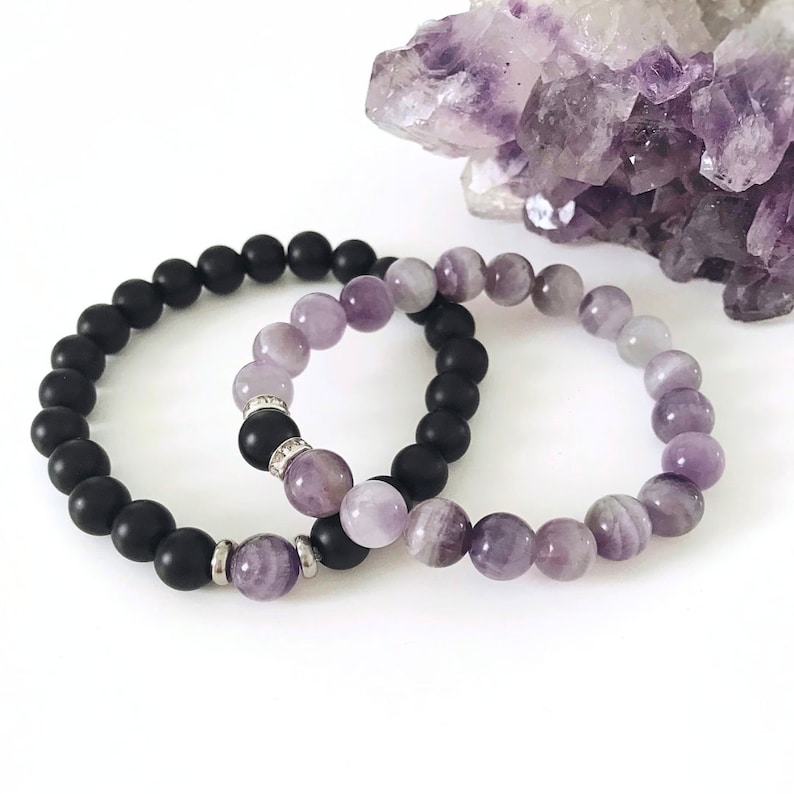 May include: Two bracelets, one black and one purple, made of beads. The purple bracelet has a gradient of light to dark purple beads.