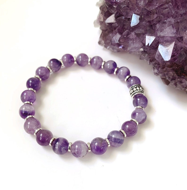 Pu&ograve; includere: Un braccialetto in ametista viola con perline d'argento. Il braccialetto &egrave; realizzato con perline rotonde e ha un ciondolo d'argento.
