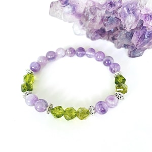 May include: A purple and green gemstone bracelet with silver accents. The bracelet is made with round and faceted beads.