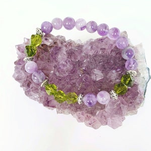 May include: A purple and green gemstone bracelet with silver accents. The bracelet is resting on a bed of purple amethyst crystals.