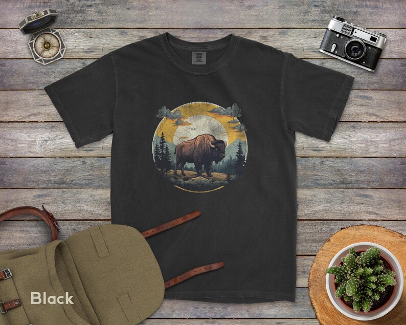 May include: A black t-shirt with a vintage-style graphic of a bison standing in a forest with a sunset in the background.