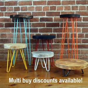 May include: Five different wooden stools with hairpin legs in various colours. The stools are arranged in a row against a brick wall. The stools are all different heights and have different coloured legs. The text "Multi buy discounts available!" is at the bottom of the image.