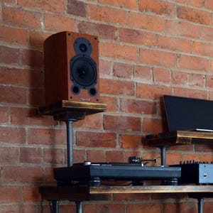 May include: A wooden shelf unit with black metal pipes, a turntable, a speaker, and a laptop on top. The speaker is mounted on a black metal pipe stand.