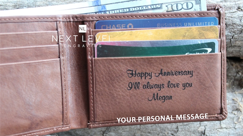 May include: A brown leather wallet with a personalized message that reads "Happy Anniversary I'll always love you Megan". The wallet has a card slot and a billfold. The wallet is open and there are credit cards inside.