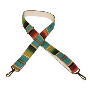 May include: A turquoise, green, red, and yellow striped adjustable strap with brass hardware. The strap is made of woven fabric and has a white canvas lining.