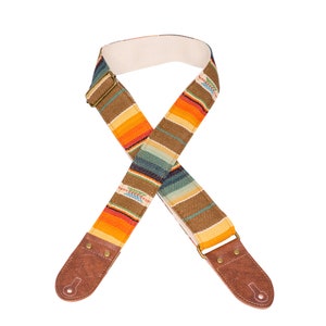 May include: A guitar strap with a colorful striped pattern in shades of orange, yellow, brown, blue, and green. The strap has brown leather ends with metal buckles.