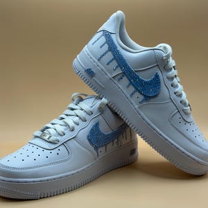 May include: White leather low-top sneakers with a blue rhinestone swoosh and drip design.