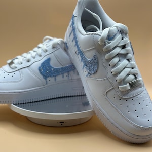 May include: White leather sneakers with a blue rhinestone swoosh and drip design.