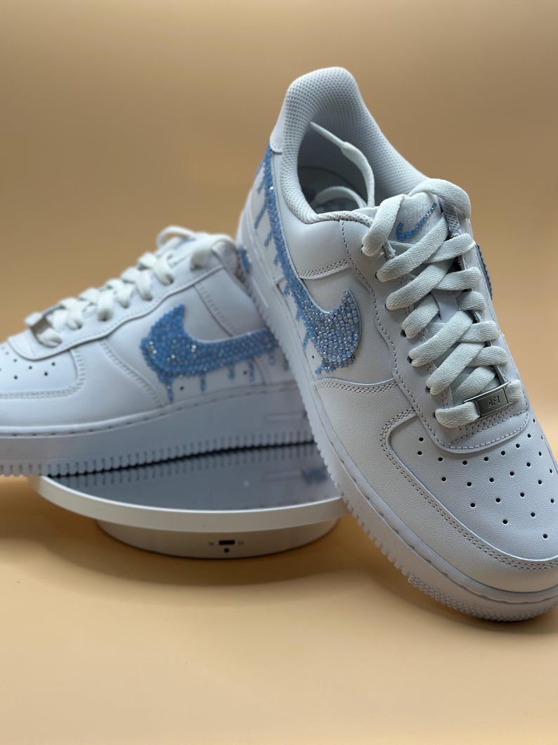May include: White leather sneakers with a blue rhinestone swoosh and drip design.
