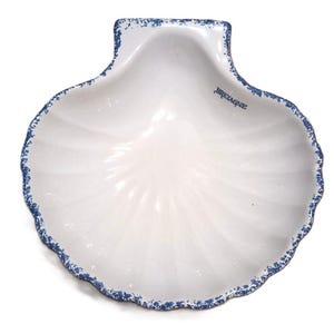 Peut inclure: Un plat en céramique blanc en forme de coquille Saint-Jacques avec un motif bleu moucheté sur les bords festonnés. Le mot BRETAGNE est imprimé en bleu foncé sur la surface intérieure du plat, qui présente des nervures radiales en relief.