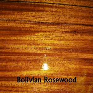 Puede incluir: Primer plano de una superficie de veta de madera rica, marrón rojiza, con un acabado brillante. La madera está etiquetada como "Bolivian Rosewood".