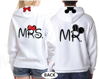 May include: White hooded sweatshirts with the words "MRS." and "MR." in black script. The "MRS." sweatshirt has a red bow with white polka dots and the "MR." sweatshirt has a black Mickey Mouse head.