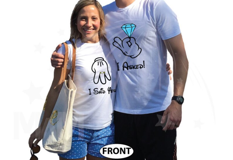 May include: A couple wearing white t-shirts with a Mickey Mouse hand graphic and the text "I Asked!" and "I Said Yes!"  The couple is standing in front of a white background.