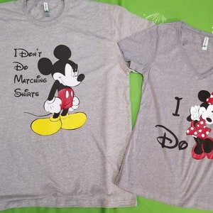 May include: Two grey t-shirts with a Mickey Mouse and Minnie Mouse design. The Mickey Mouse shirt says "I Don't Do Matching Shirts". The Minnie Mouse shirt says "I Do".