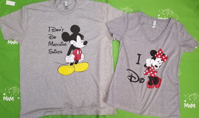May include: Two grey t-shirts with a Mickey Mouse and Minnie Mouse design. The Mickey Mouse shirt says "I Don't Do Matching Shirts". The Minnie Mouse shirt says "I Do".