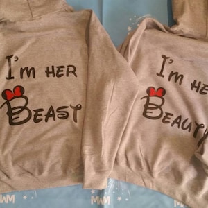 May include: Two gray hooded sweatshirts with a red heart and text that reads "I'm her Beast" and "I'm her Beauty".