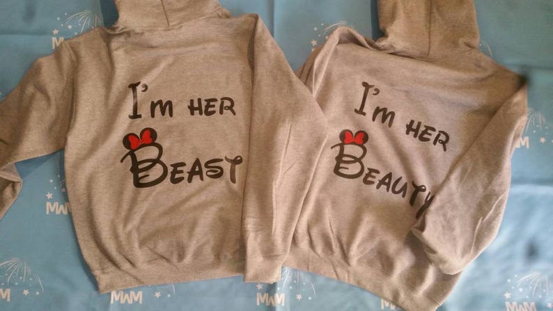 May include: Two gray hooded sweatshirts with a red heart and text that reads "I'm her Beast" and "I'm her Beauty".