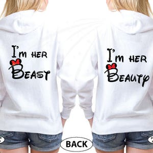 May include: Two white hooded sweatshirts with a red heart and text that reads "I'm her Beast" and "I'm her Beauty".