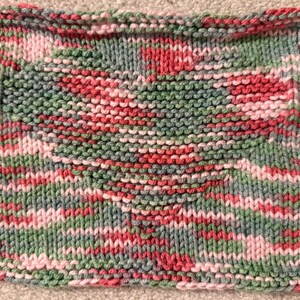 Puede incluir: Un cuadrado tejido a mano en tonos rosa, verde y gris. El hilo es una mezcla de colores, creando un diseño texturizado y estampado. Los bordes están cuidadosamente acabados, mostrando la artesanía de la pieza.