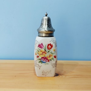 Könnte beinhalten: Ein weißer Zuckerstreuer aus Keramik mit einem silbernen Deckel und einem Blumendesign mit gelben, roten und rosa Blüten.