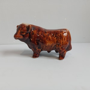 May include: A brown ceramic bull figurine with a glossy finish. The bull is depicted in a standing position, showcasing its muscular build and horns. The figurine is a decorative item, likely for display.