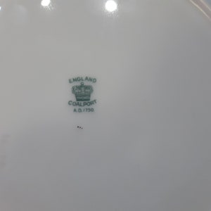 May include: A white porcelain plate with a green and black Coalport mark. The mark includes a crown, the words "England" and "Coalport", and the date "A.D. 1750".