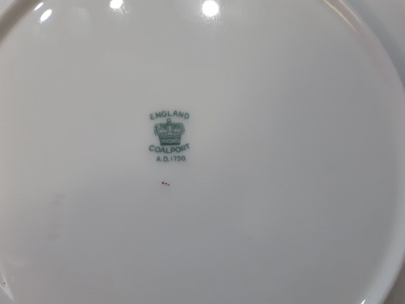 May include: A white porcelain plate with a green and black Coalport mark. The mark includes a crown, the words "England" and "Coalport", and the date "A.D. 1750".